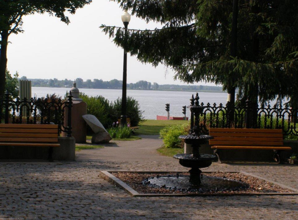 A view of the St. Lawrence River with walkway, fountain and bench in foreground